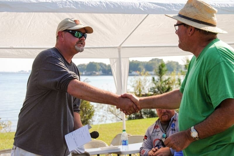 Two men shaking hands in front of a tent.