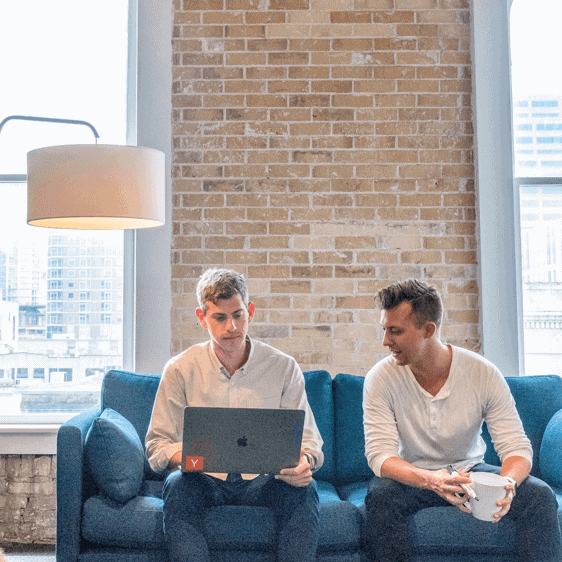 Two men sitting on a couch looking at a laptop.