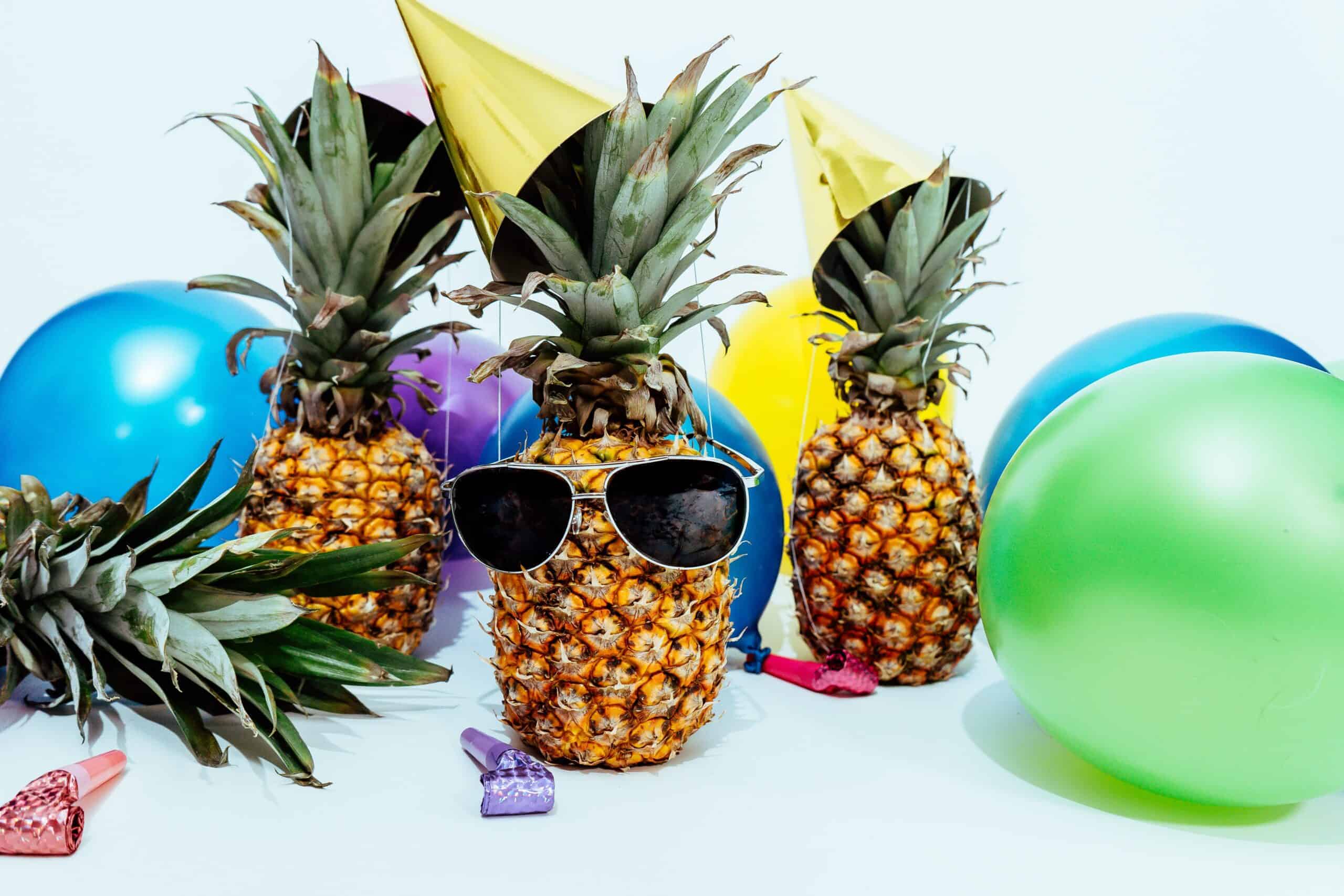 A group of pineapples with sunglasses and balloons.