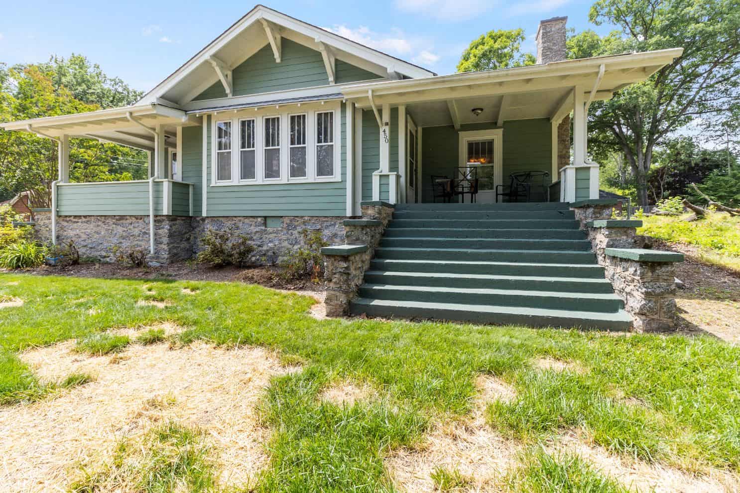 A green house with steps leading up to a grassy yard.