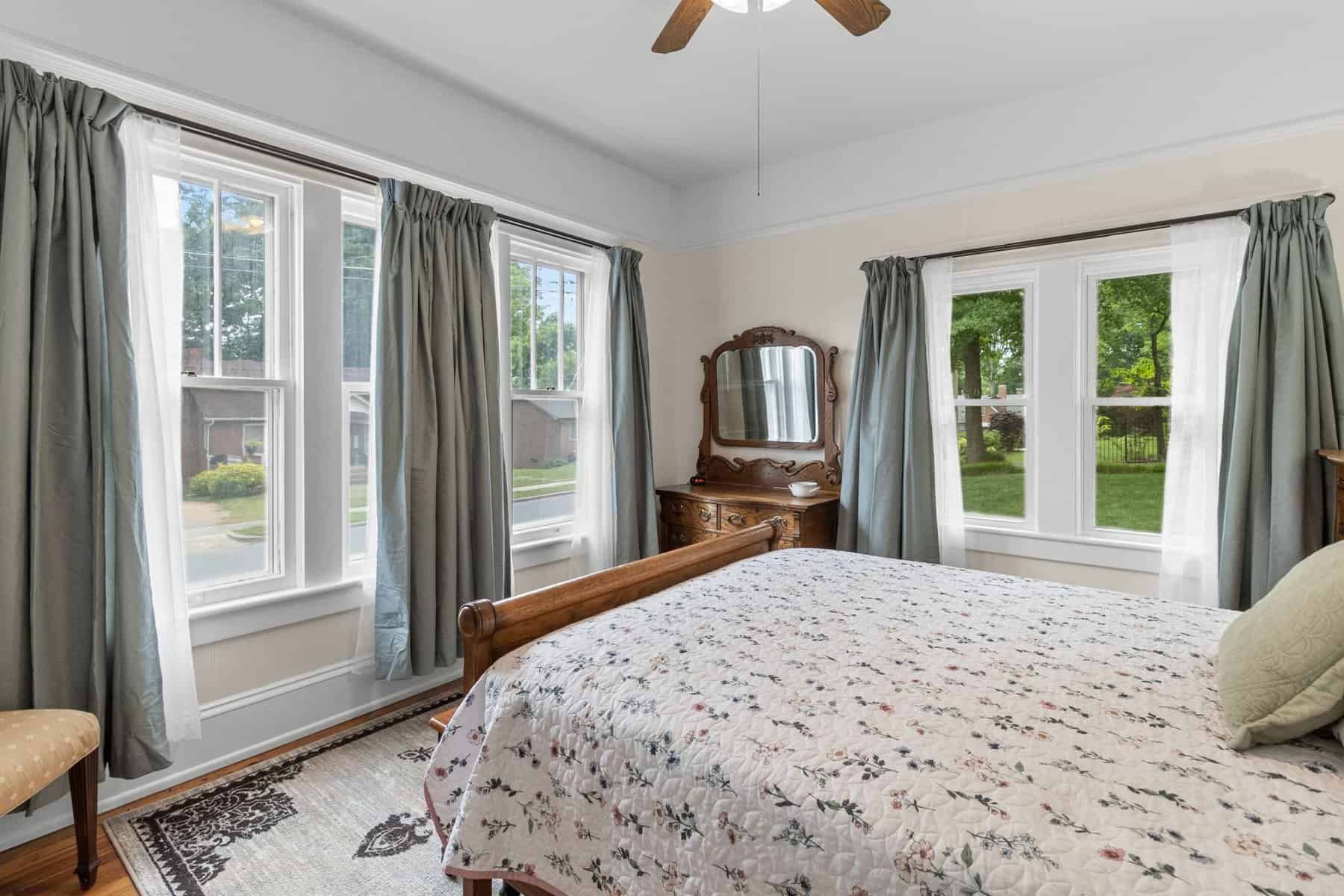 A bed in a bedroom with windows and a fan.