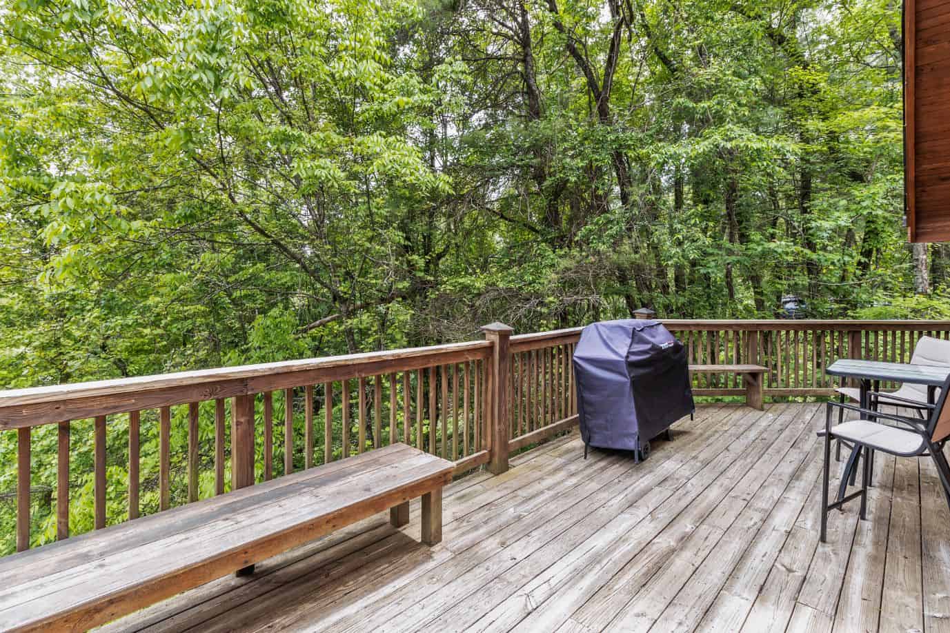 A deck overlooking a wooded area with a grill.