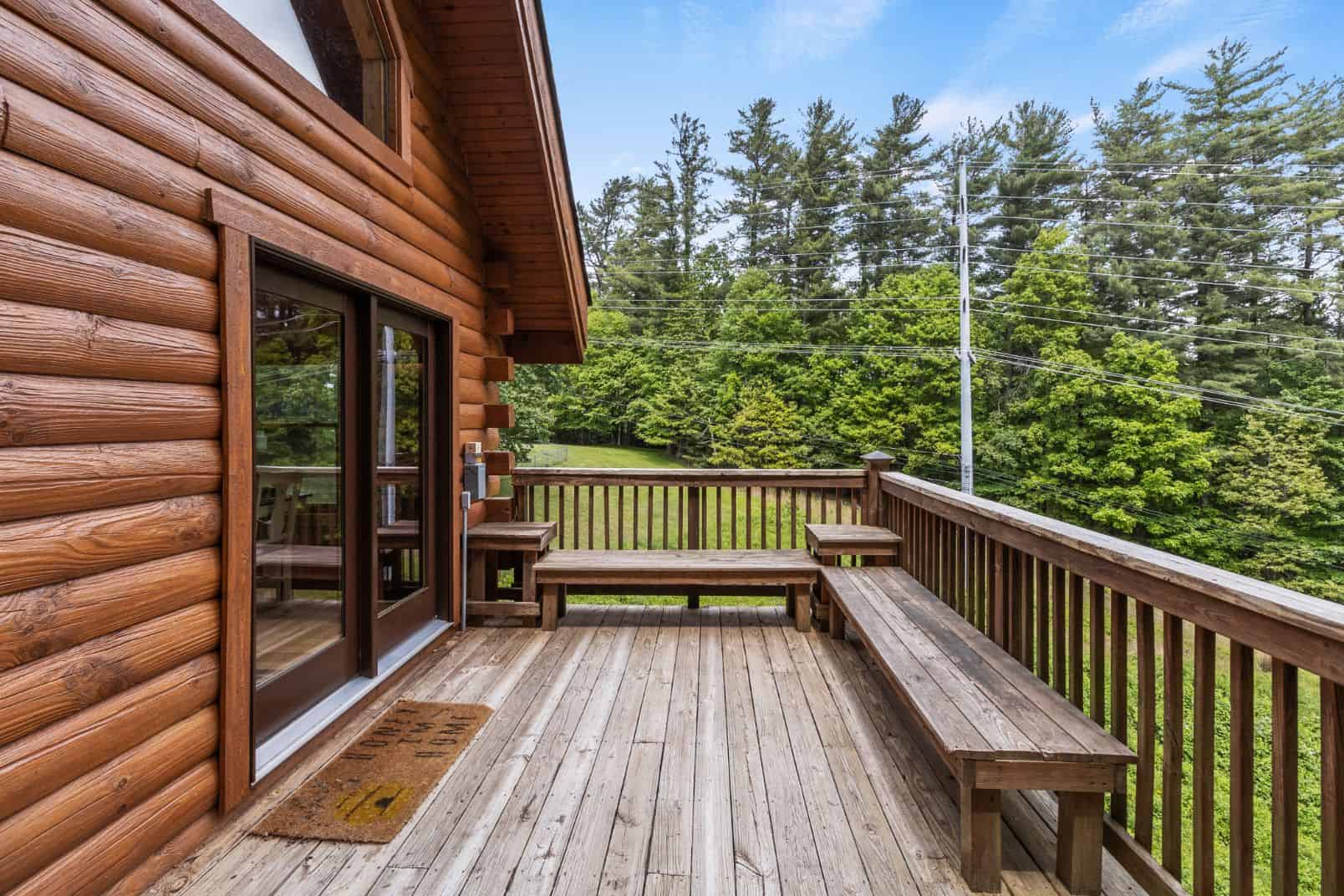 The deck of a log cabin overlooking a wooded area.