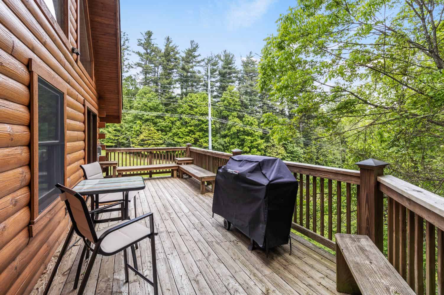 The deck of a log cabin with a grill.