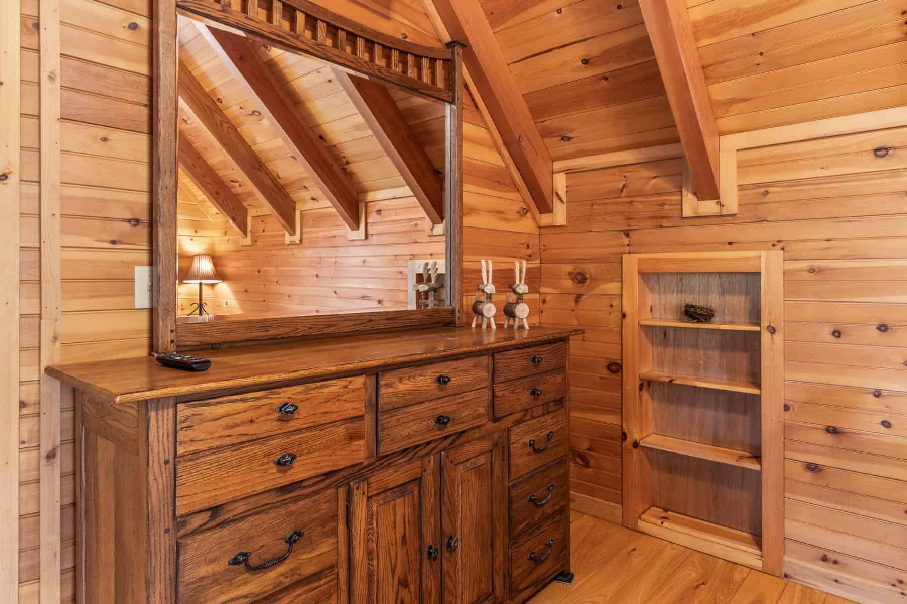 A bedroom in a log cabin with a dresser and mirror.