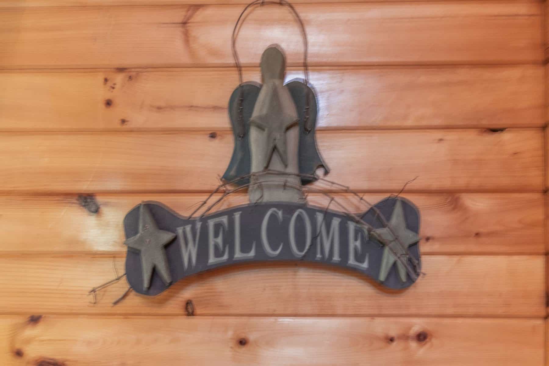 A wooden welcome sign hangs on the wall of a cabin.