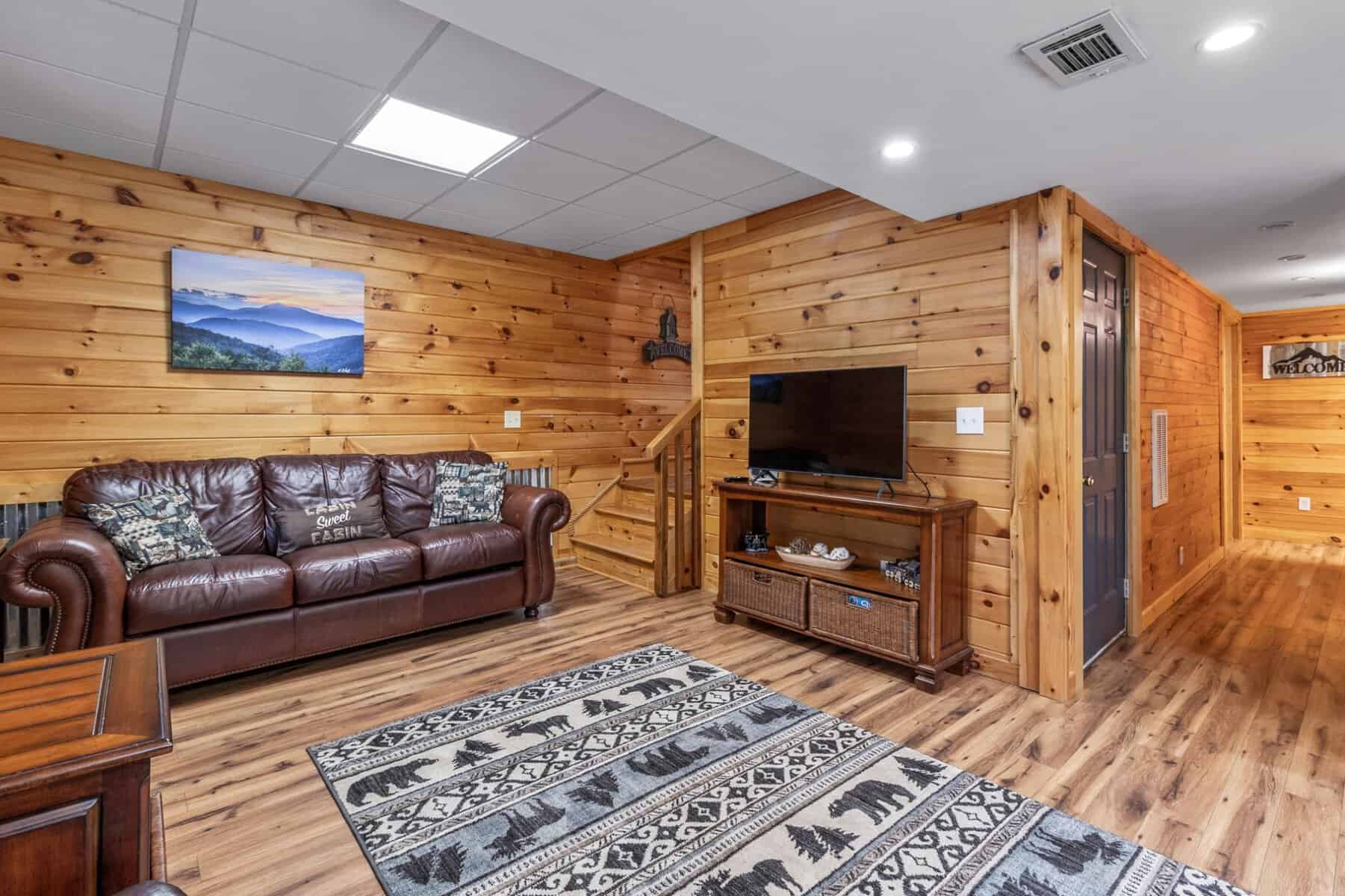 A living room in a log cabin with leather couches and a tv.