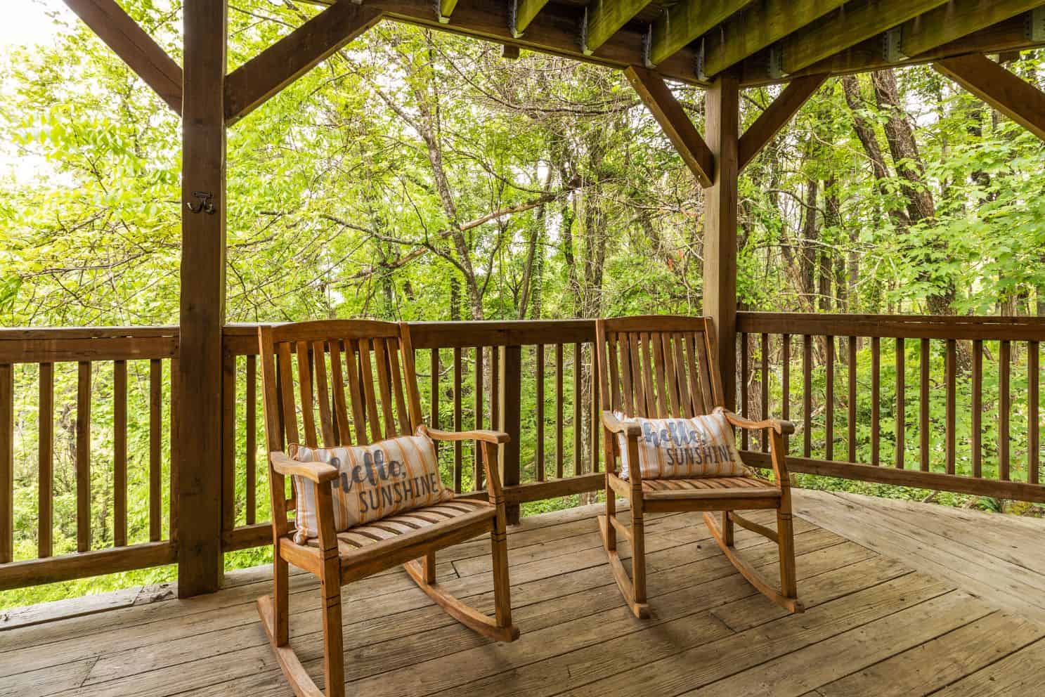 Two rocking chairs on a porch overlooking a wooded area.