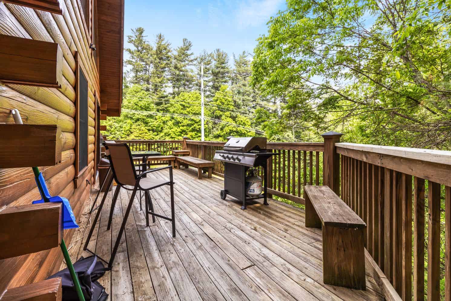 The deck of a cabin with a grill and chairs.