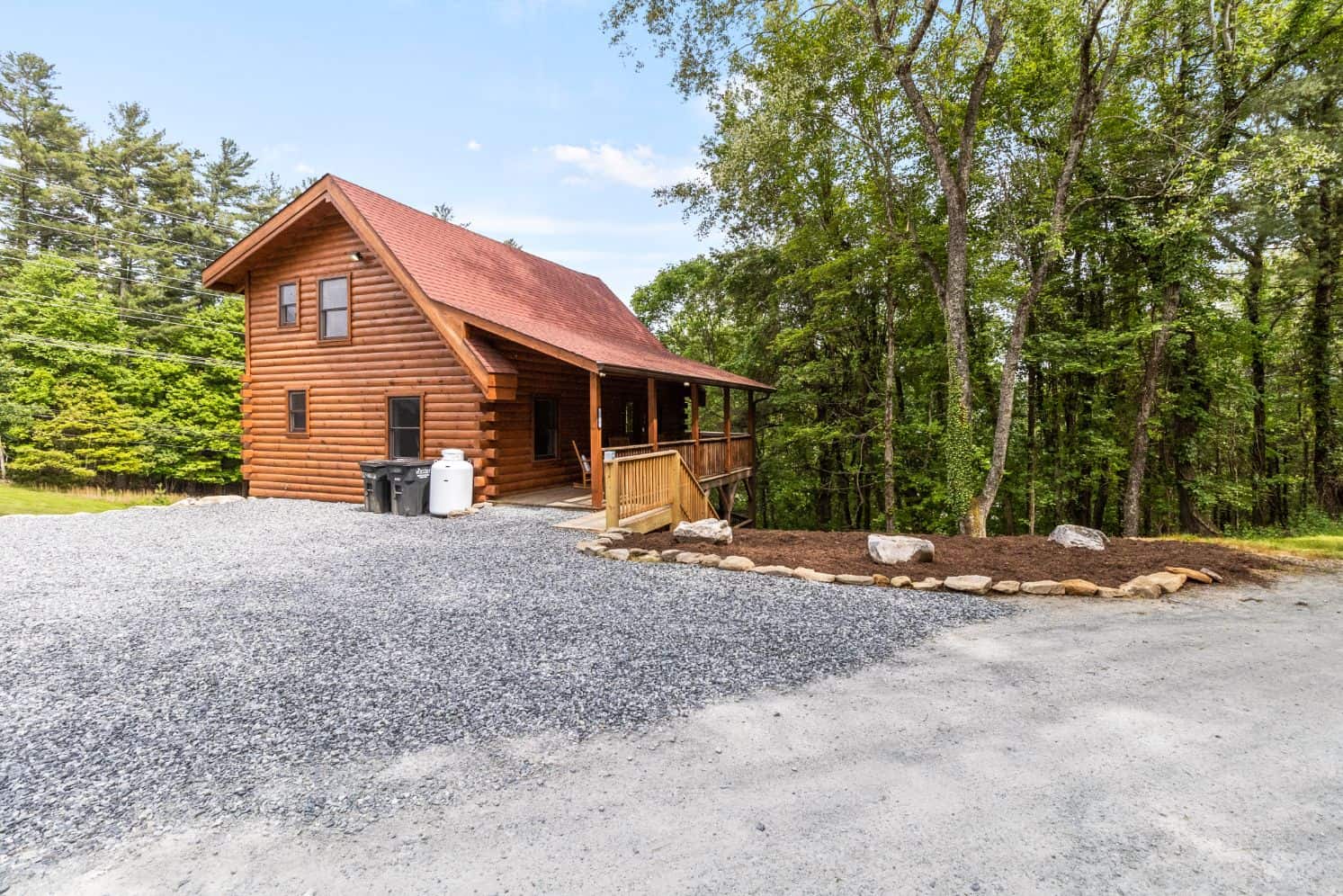 A log cabin in the woods with a gravel driveway.