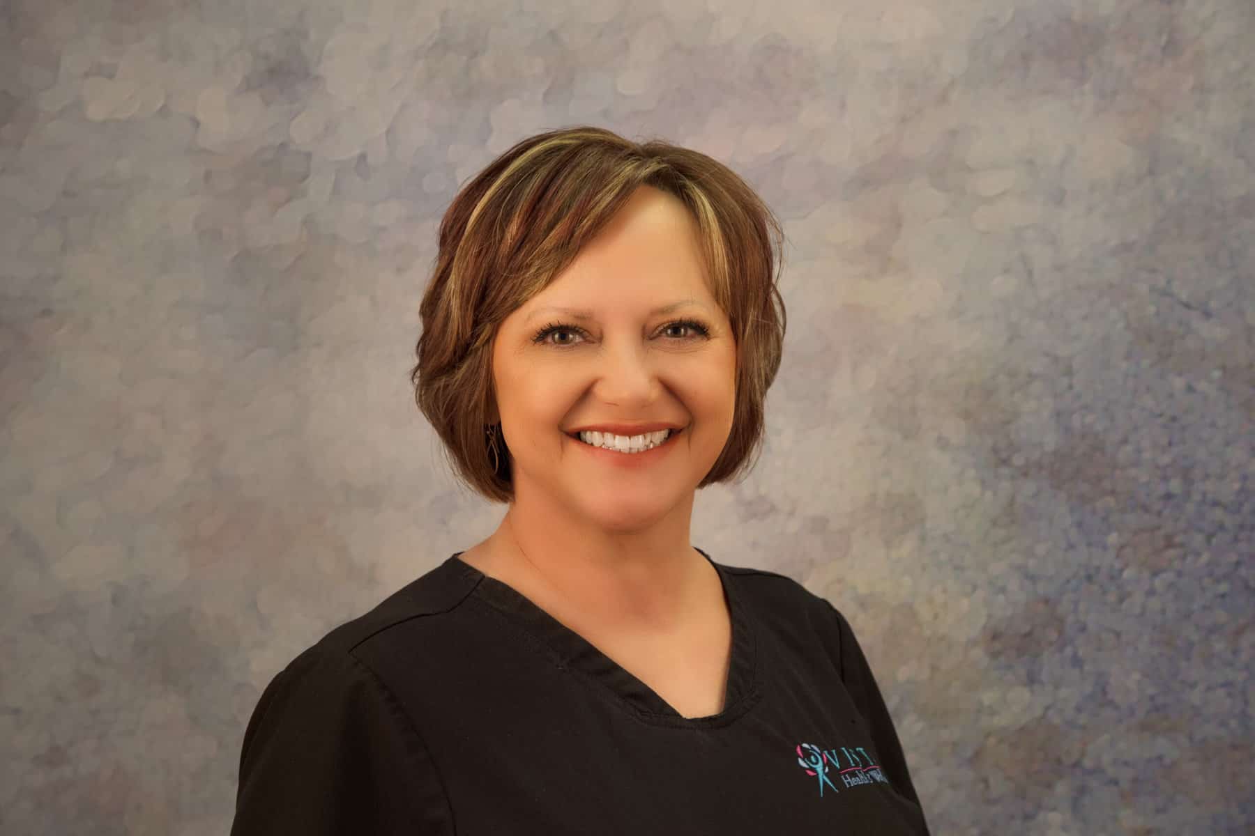 A smiling woman in a black scrub shirt.