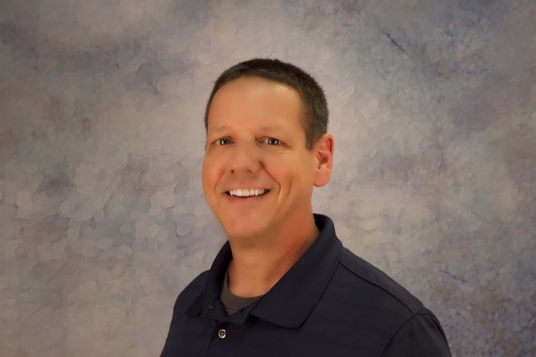 A man smiling in front of a blue background.