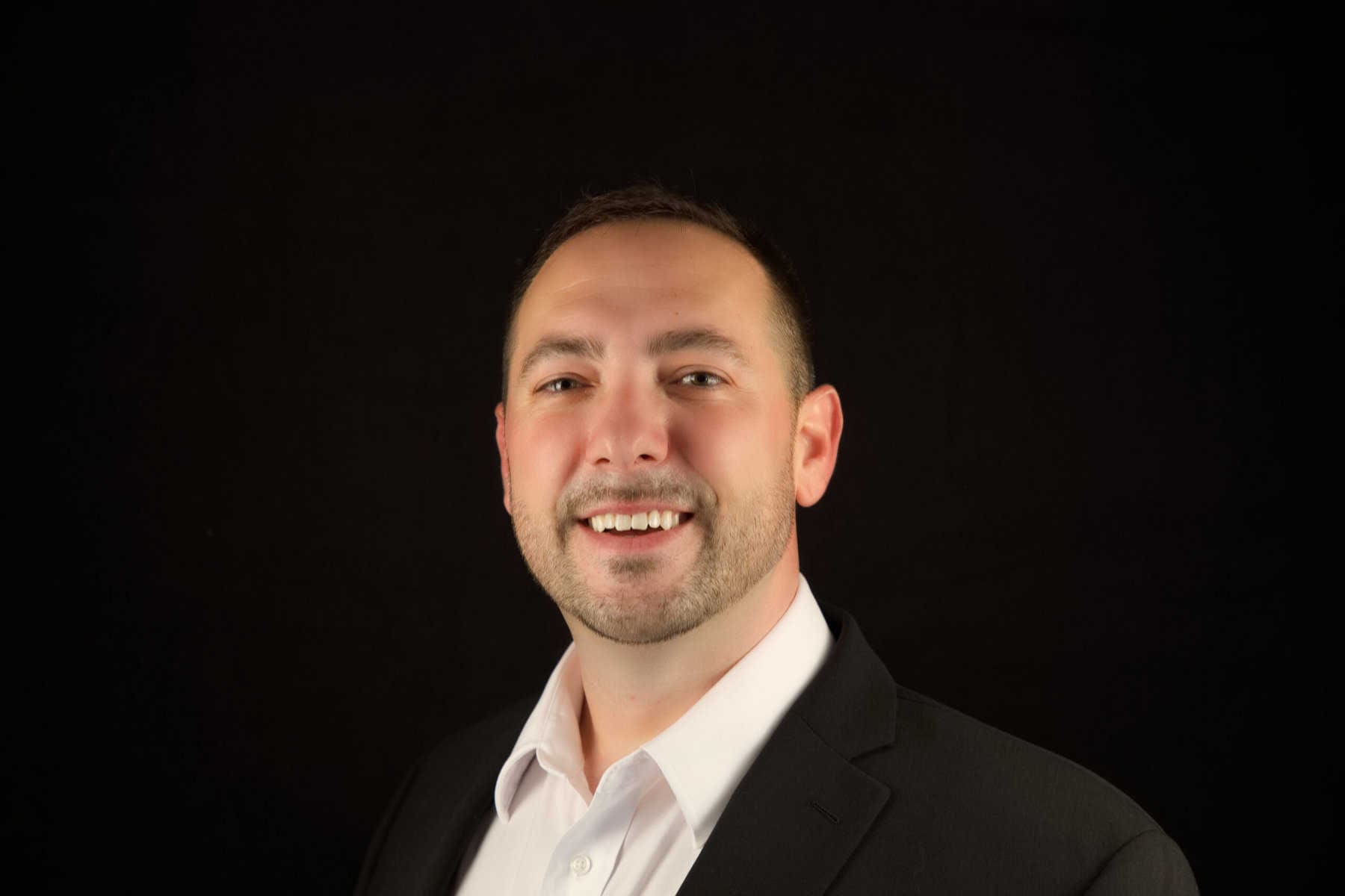 A man in a suit smiling in front of a black background.