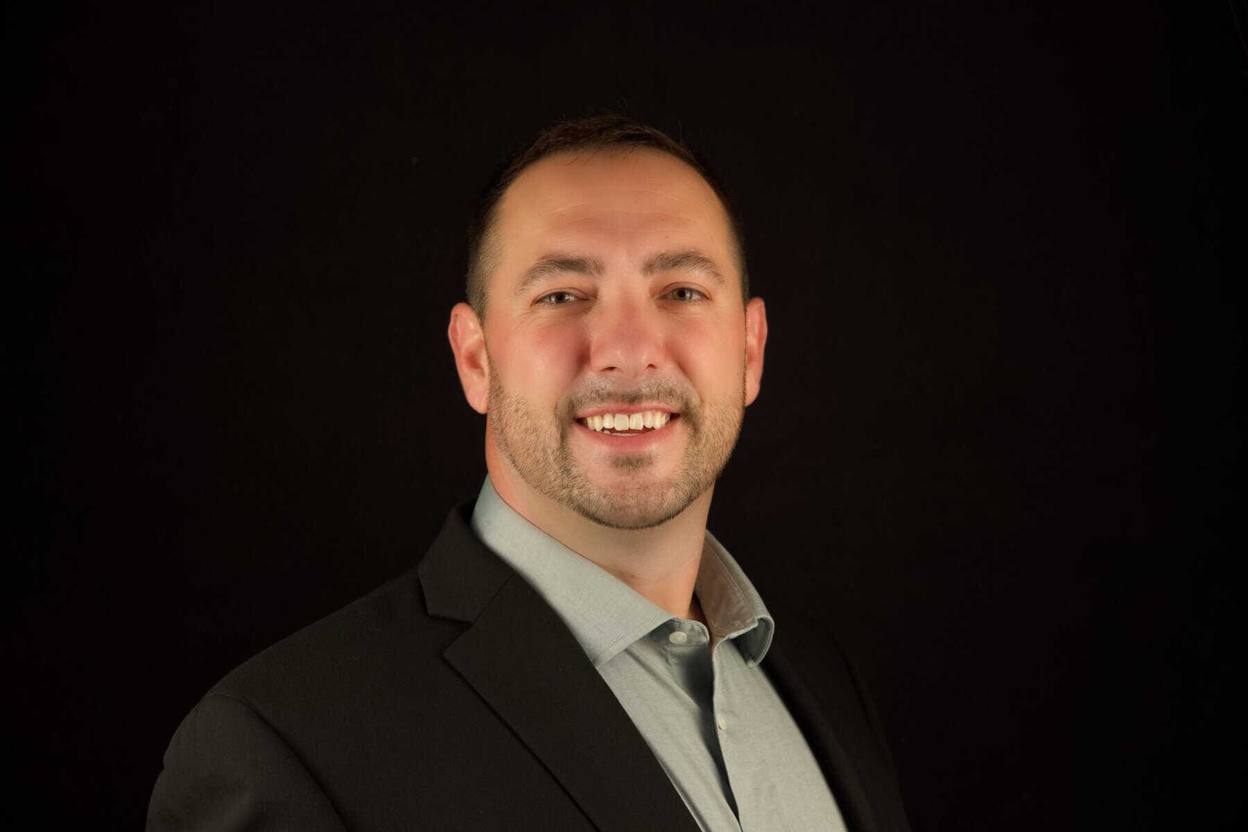 A man in a suit smiling in front of a black background.