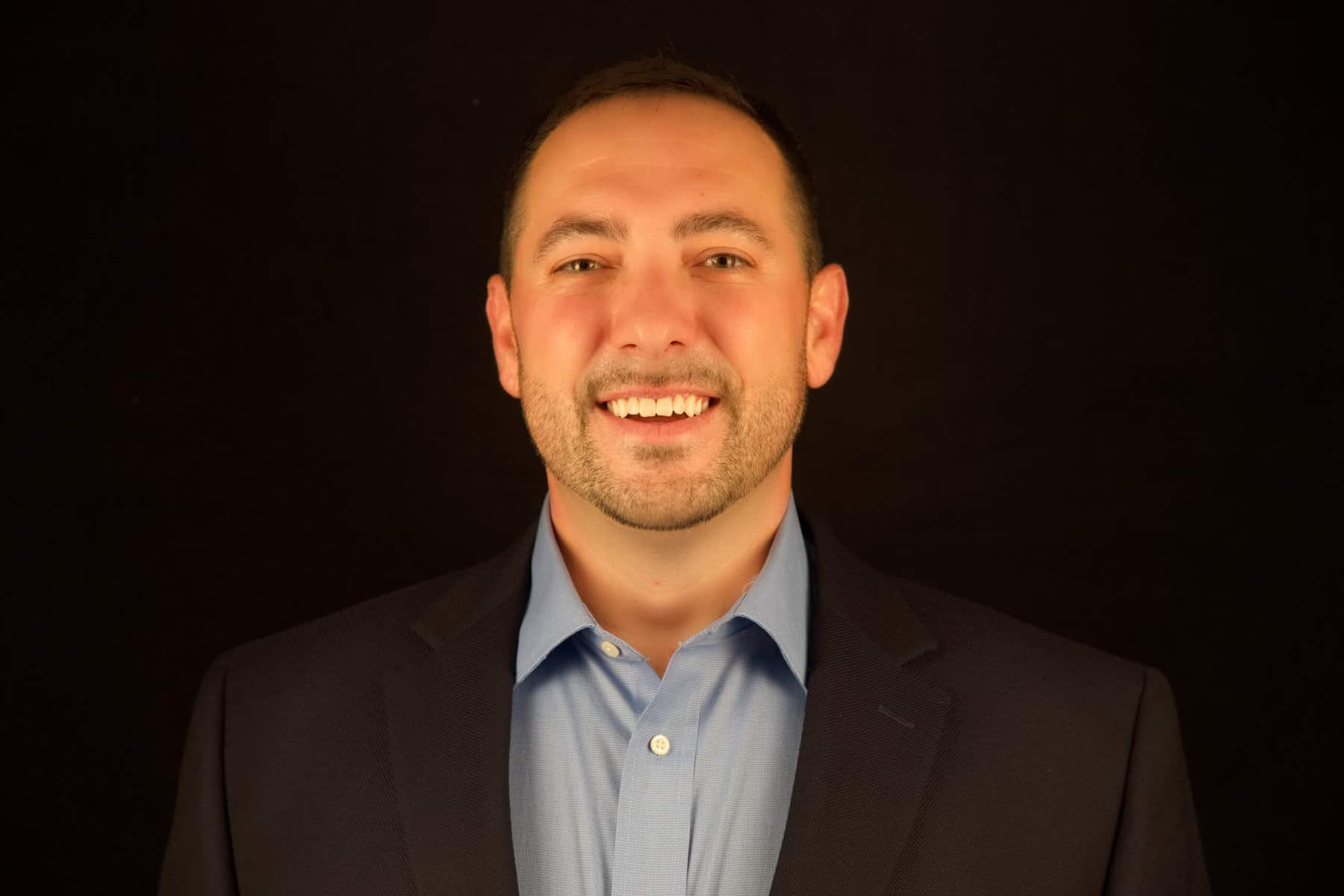 A man in a suit smiling in front of a black background.