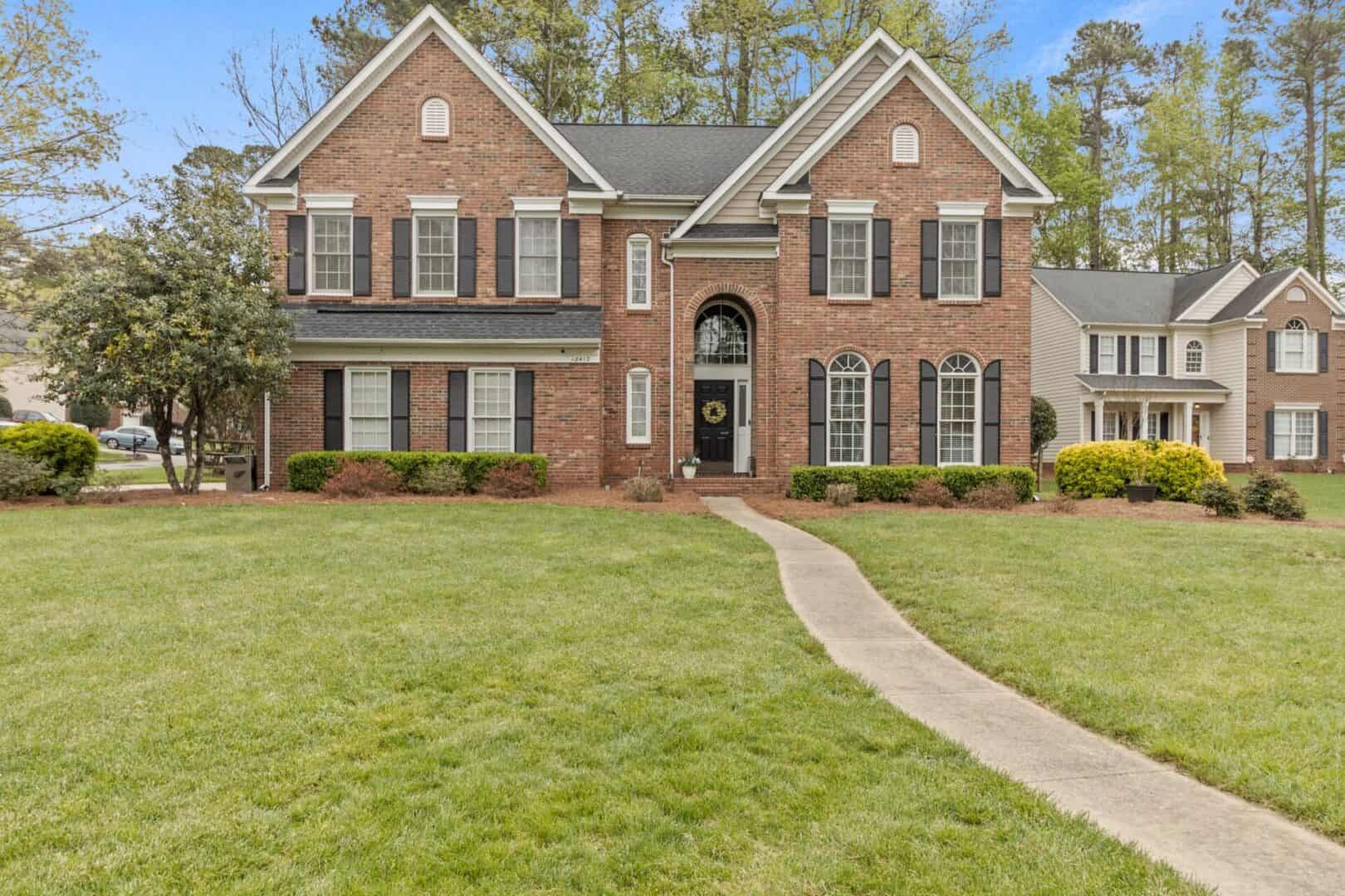 A brick home with grass and trees in the front yard.