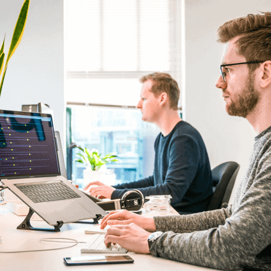 Two men sitting at a desk working on their laptops.