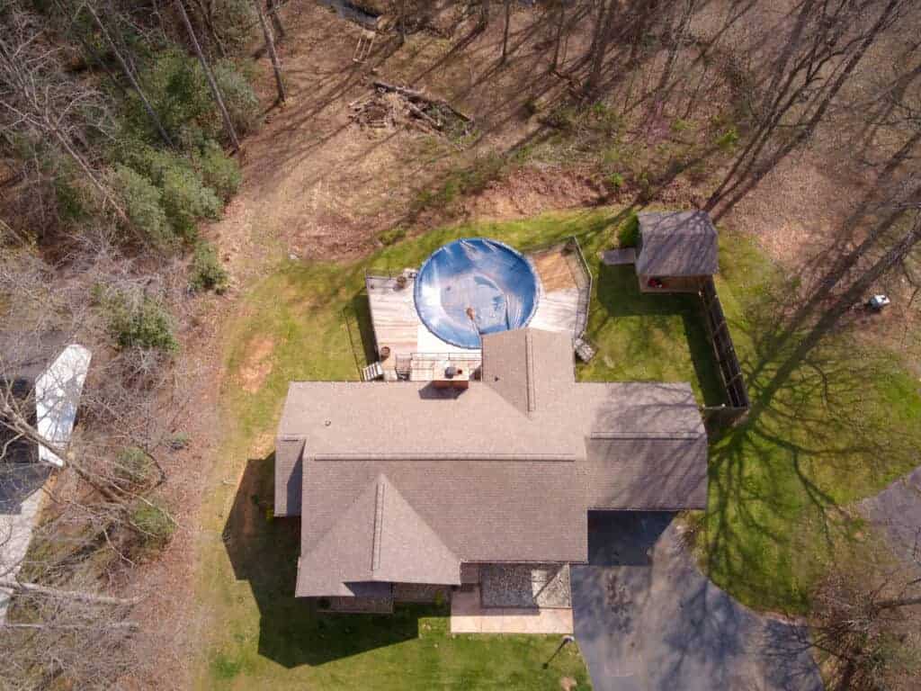 An aerial view of a home with a pool in the woods.