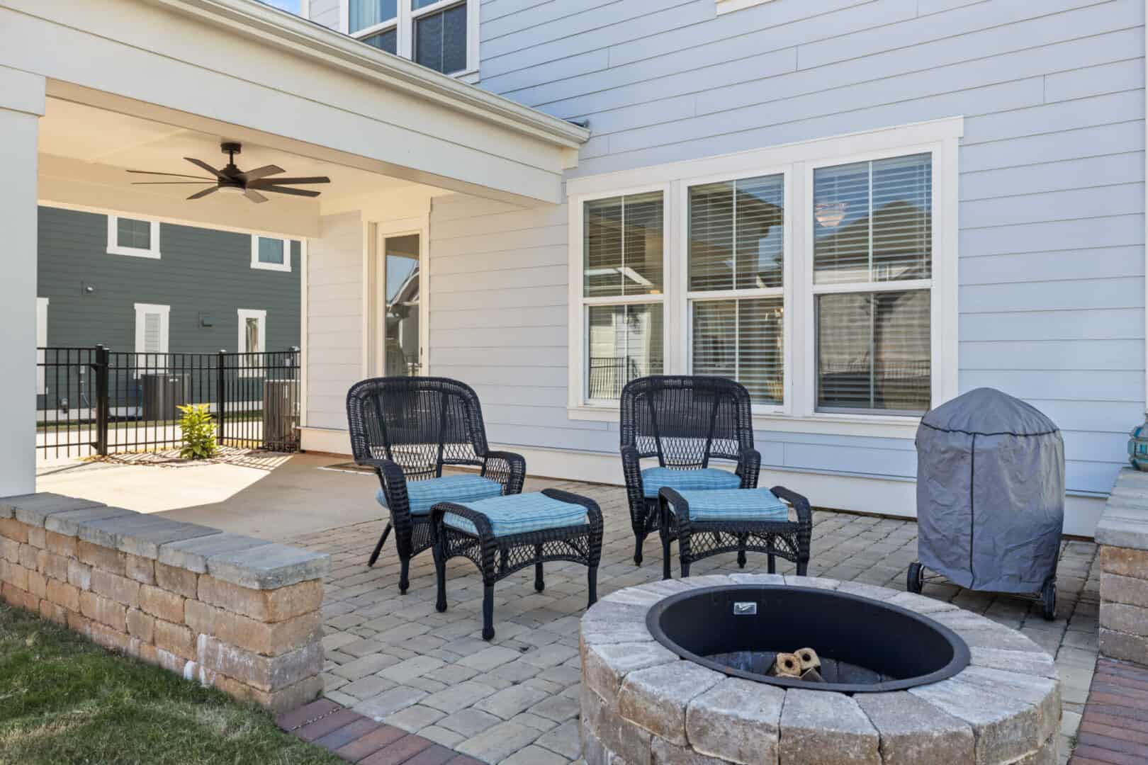 A patio with chairs and a fire pit in front of a home.