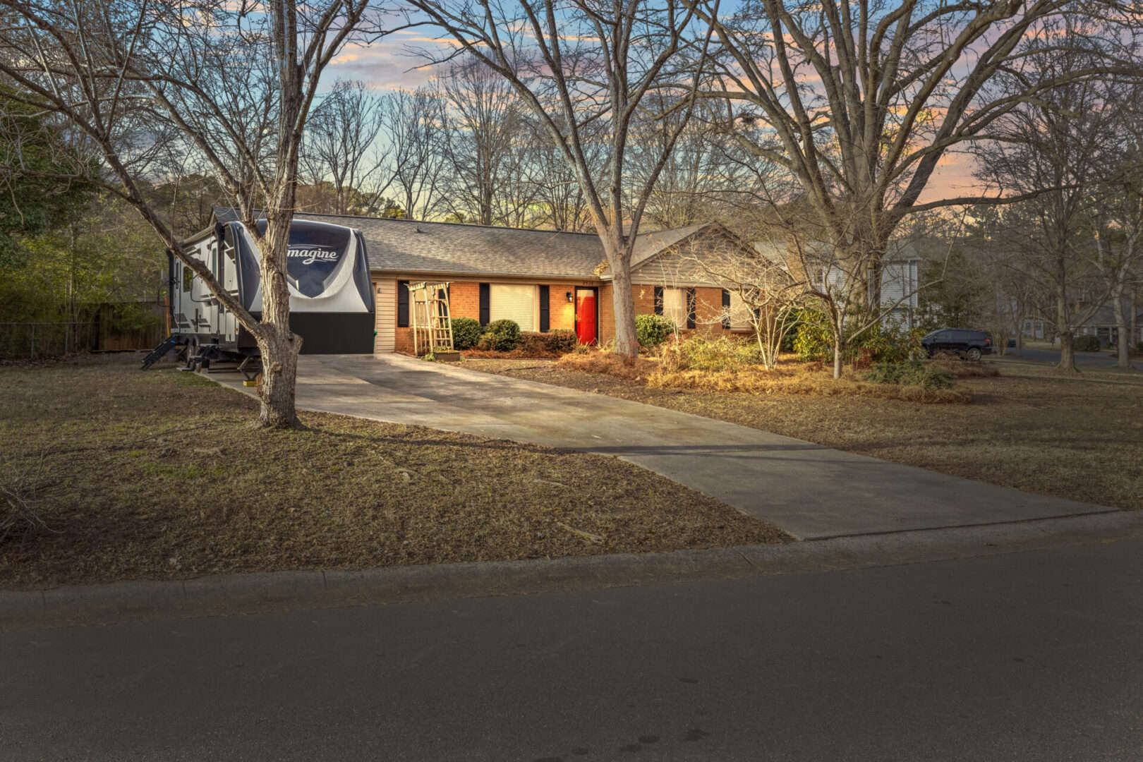 A home with a driveway and trees in front of it.